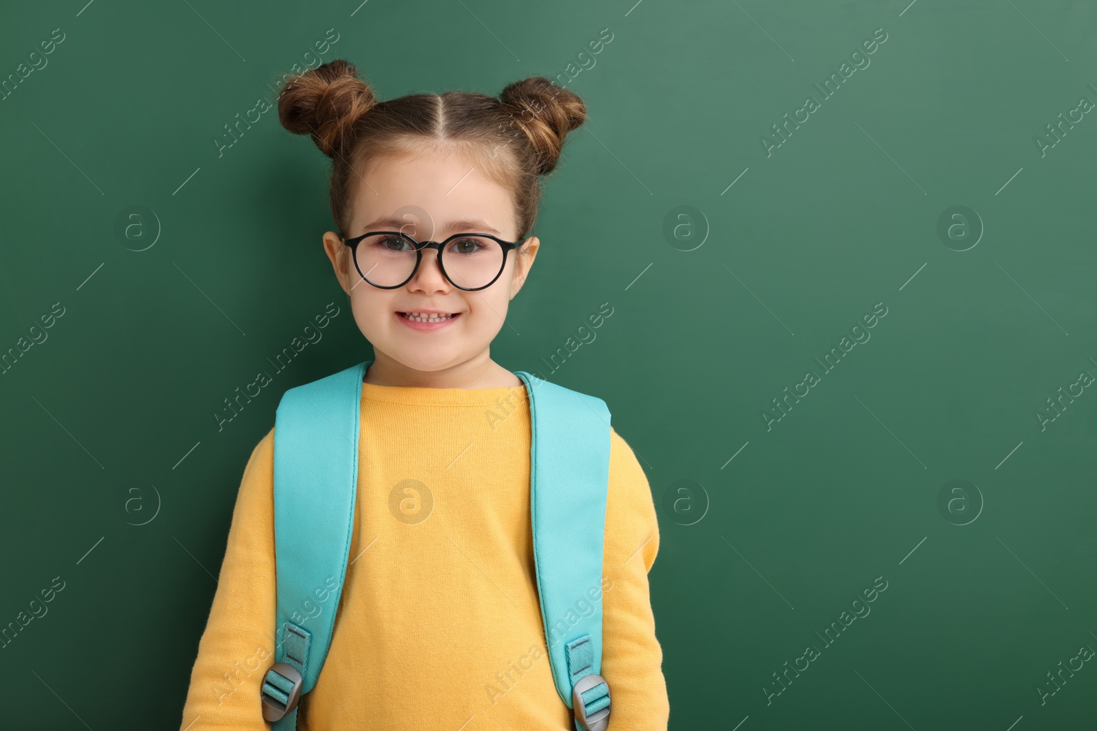 Photo of Happy little school child with backpack near chalkboard. Space for text