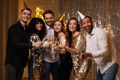 Blurred view of happy friends clinking glasses of sparkling wine at birthday party indoors