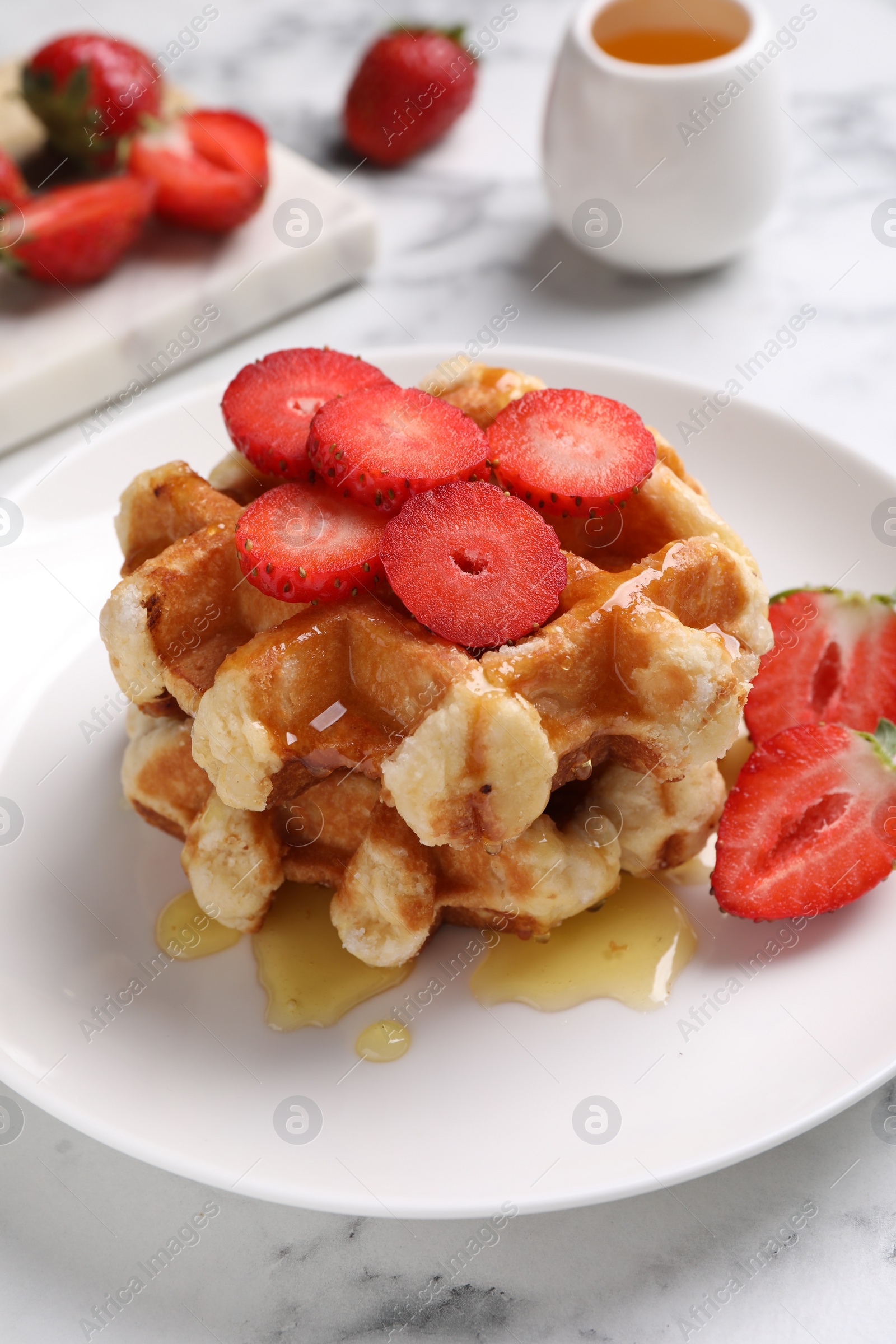 Photo of Delicious Belgian waffles with strawberries and honey on white marble table, closeup