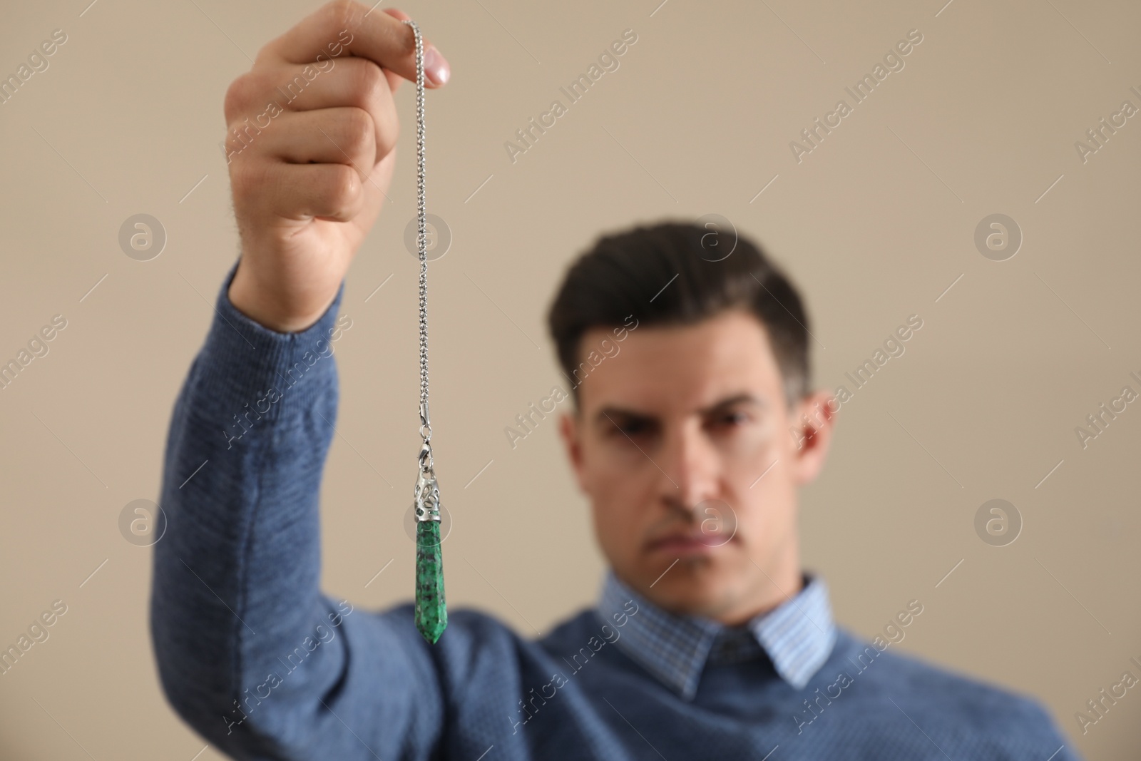 Photo of Psychotherapist with pendulum on beige background. Hypnotherapy session
