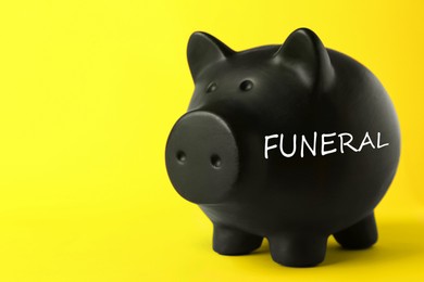 Image of Money for funeral expenses. Black piggy bank on yellow background, space for text