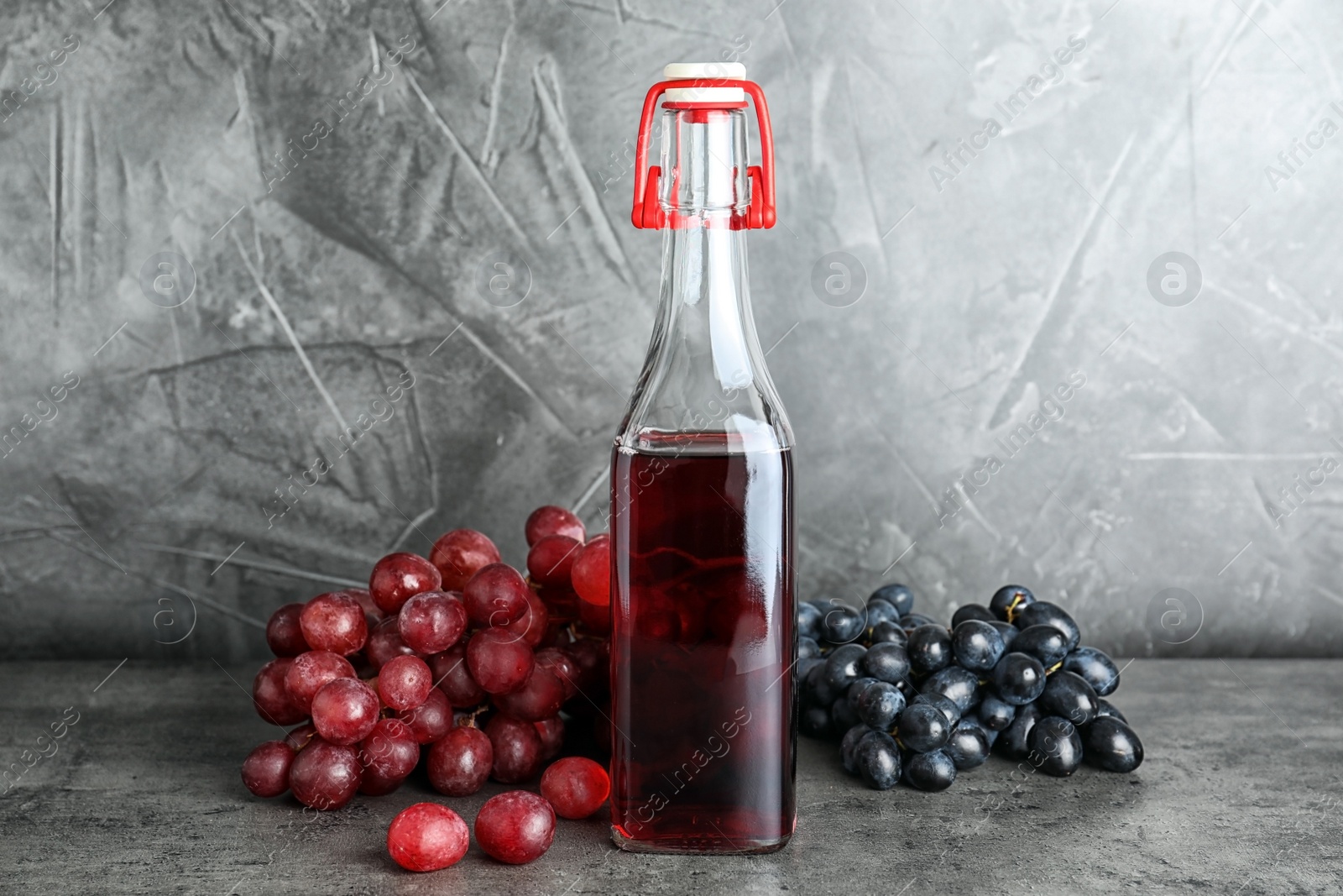 Photo of Bottle with wine vinegar and fresh grapes on gray table