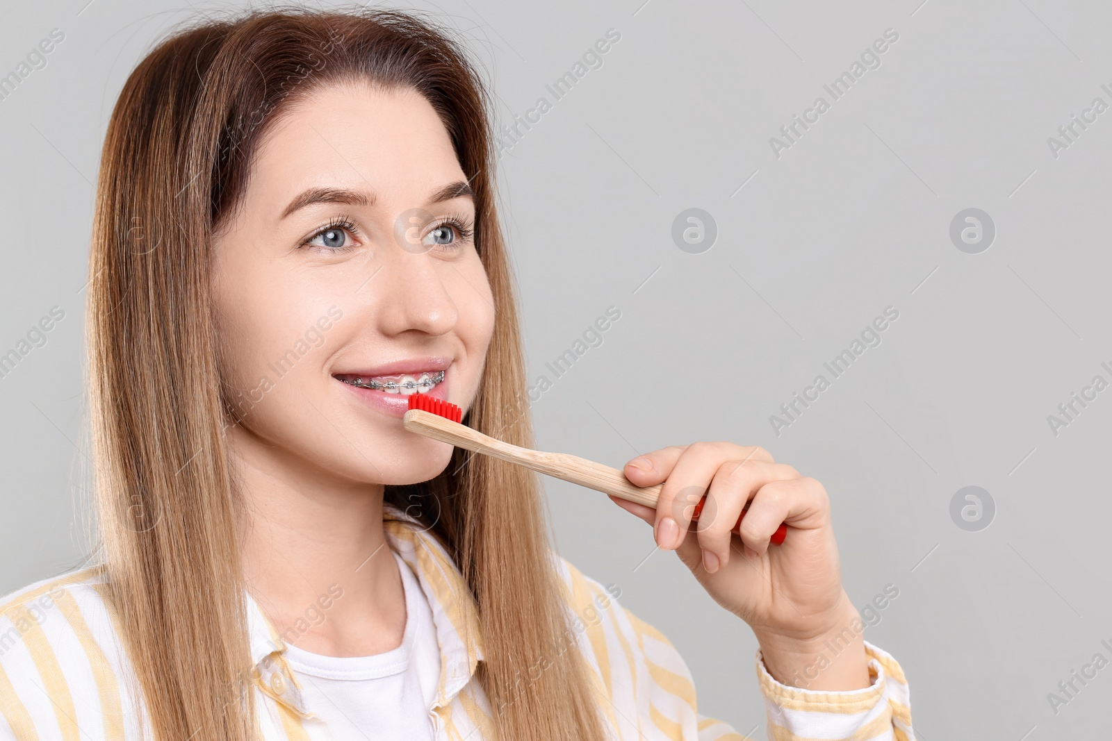 Photo of Smiling woman with dental braces cleaning teeth on grey background. Space for text