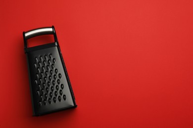 Photo of Modern black grater on red background, top view. Space for text