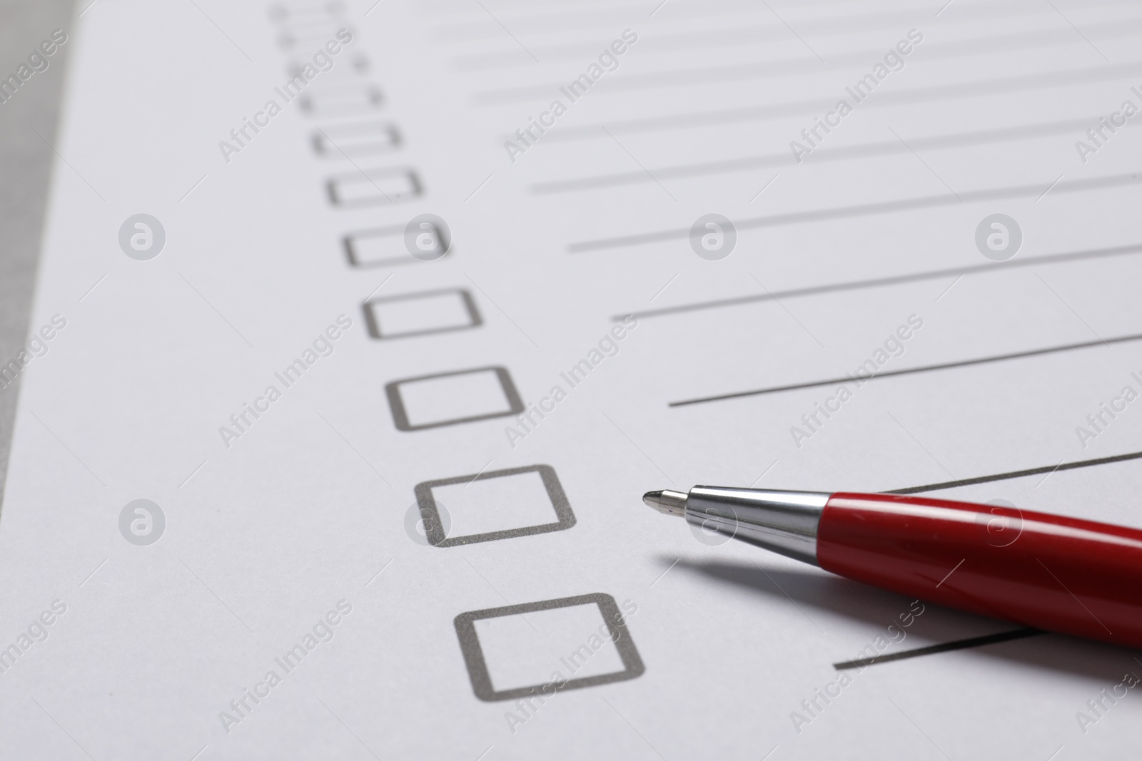 Photo of Paper sheet with checkboxes and pen on light grey table, closeup. Checklist