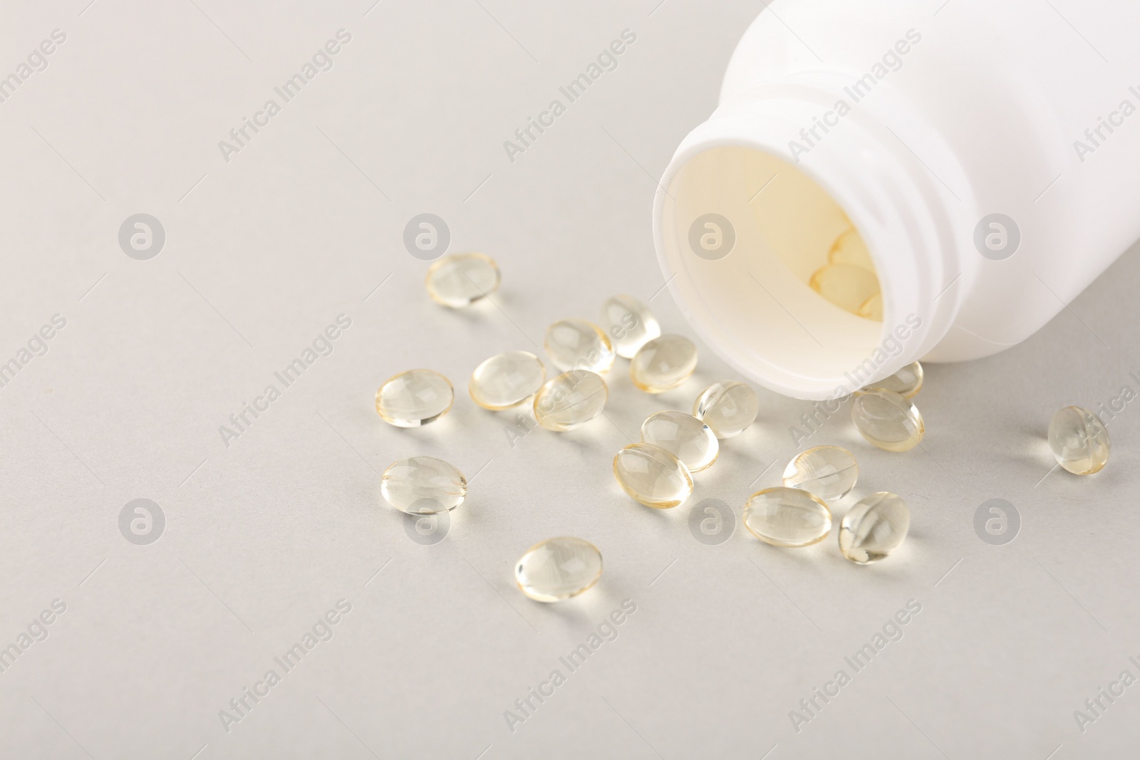 Photo of Vitamin capsules and bottle on light grey background, closeup. Space for text