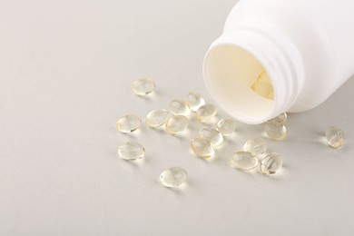 Vitamin capsules and bottle on light grey background, closeup. Space for text