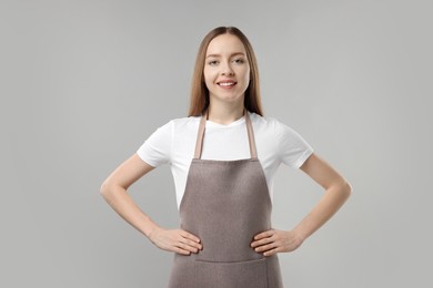 Beautiful young woman wearing kitchen apron on grey background. Mockup for design