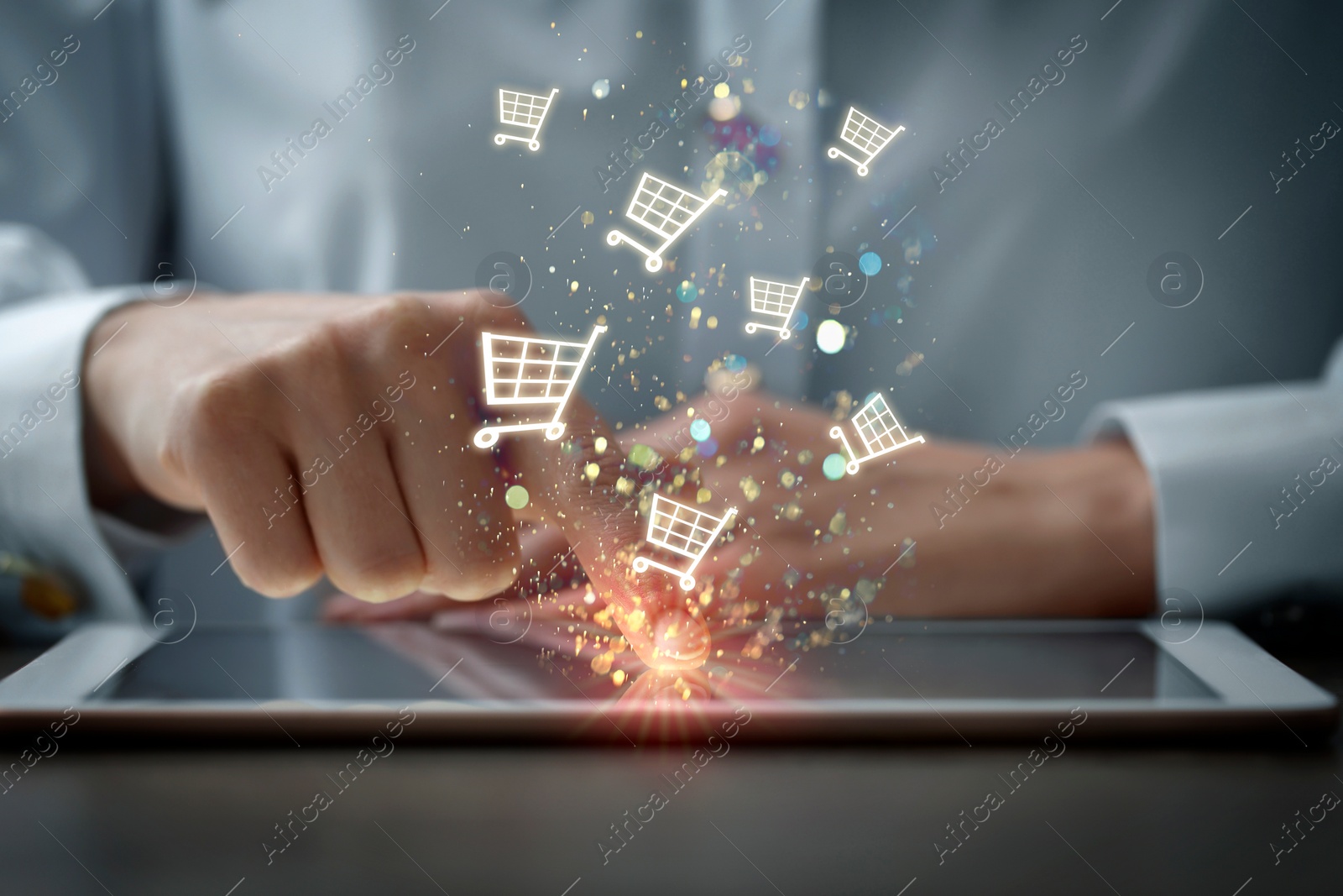 Image of Woman using tablet for online purchases at table, closeup. Shopping cart icons flying out of device screen