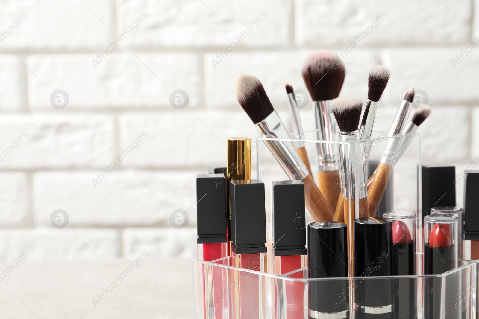Photo of Lipstick holder with different makeup products on table against brick wall, closeup. Space for text