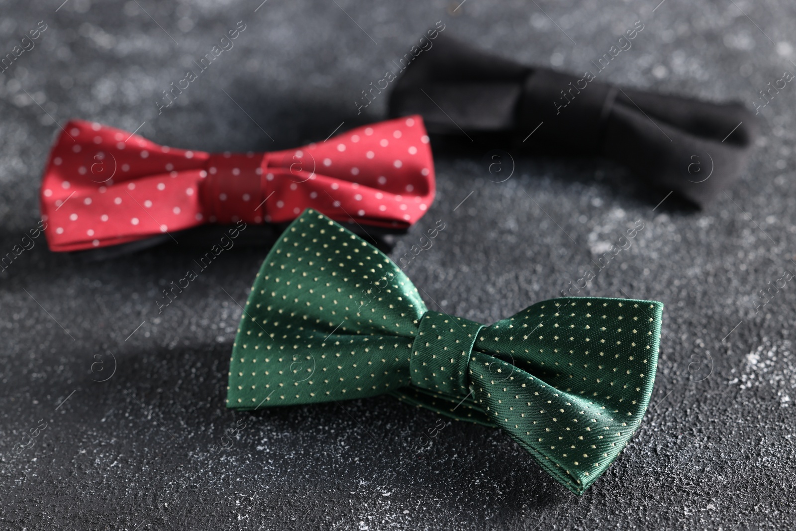 Photo of Stylish color bow ties on black textured background, closeup