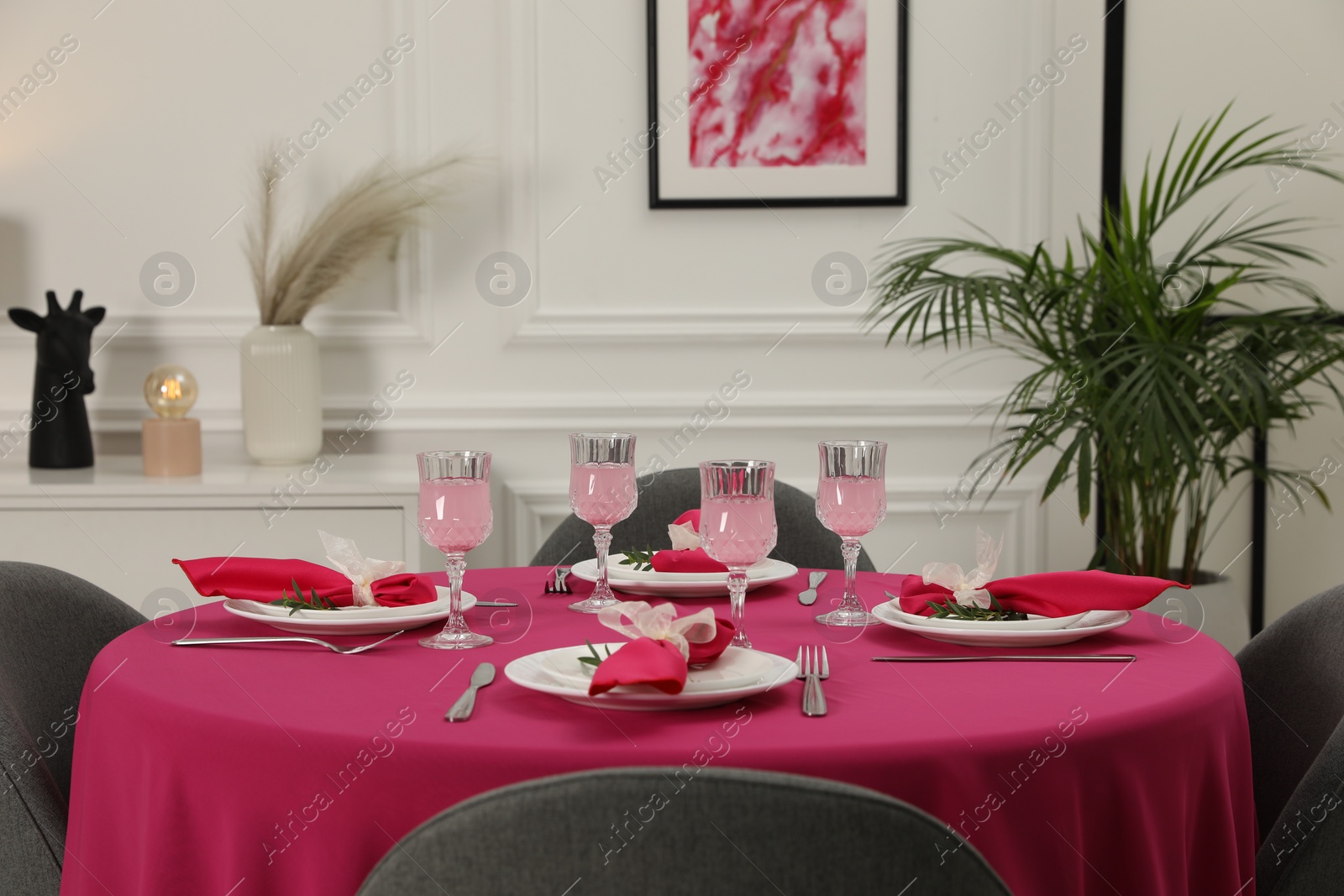 Photo of Color accent table setting. Glasses, plates, cutlery and pink napkins on table indoors