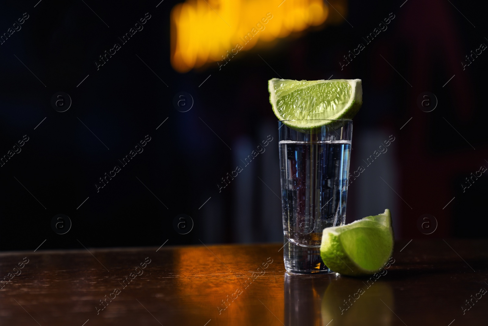 Photo of Mexican Tequila shot with lime slices on wooden bar counter. Space for text