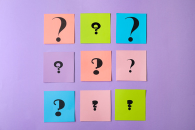 Paper cards with question marks on violet background, flat lay