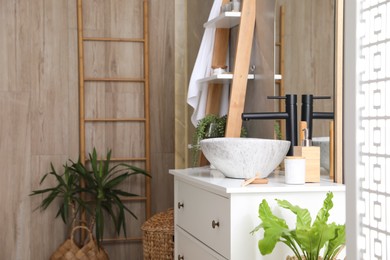 Photo of Chest of drawers with sink and beautiful green houseplants in bathroom. Interior design