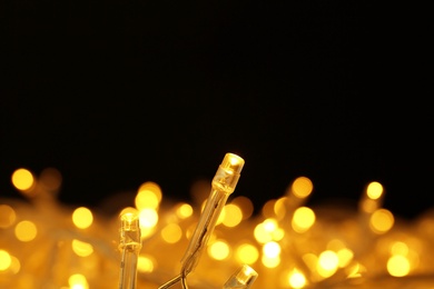 Photo of Glowing Christmas lights on black background, closeup. Space for text