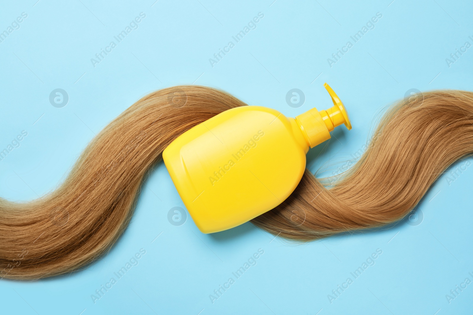 Photo of Blank bottle of cosmetic product and hair on light blue background, flat lay. Space for design