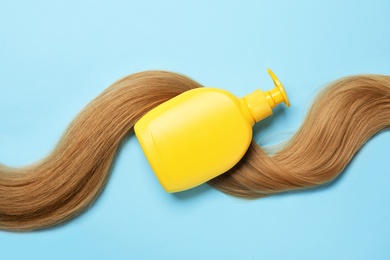 Photo of Blank bottle of cosmetic product and hair on light blue background, flat lay. Space for design