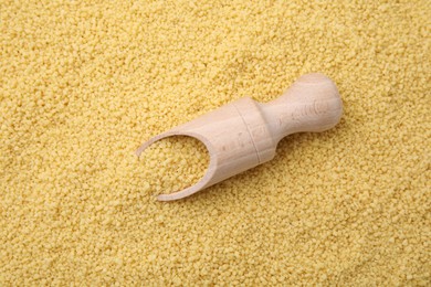 Photo of Wooden scoop and uncooked organic couscous as background, top view