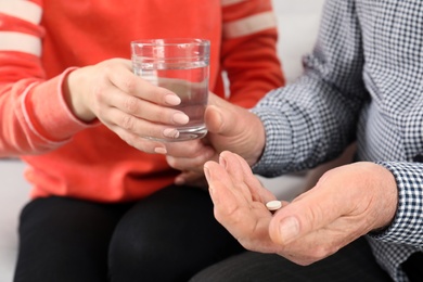 Photo of Woman giving glass of water to senior man with pill, closeup