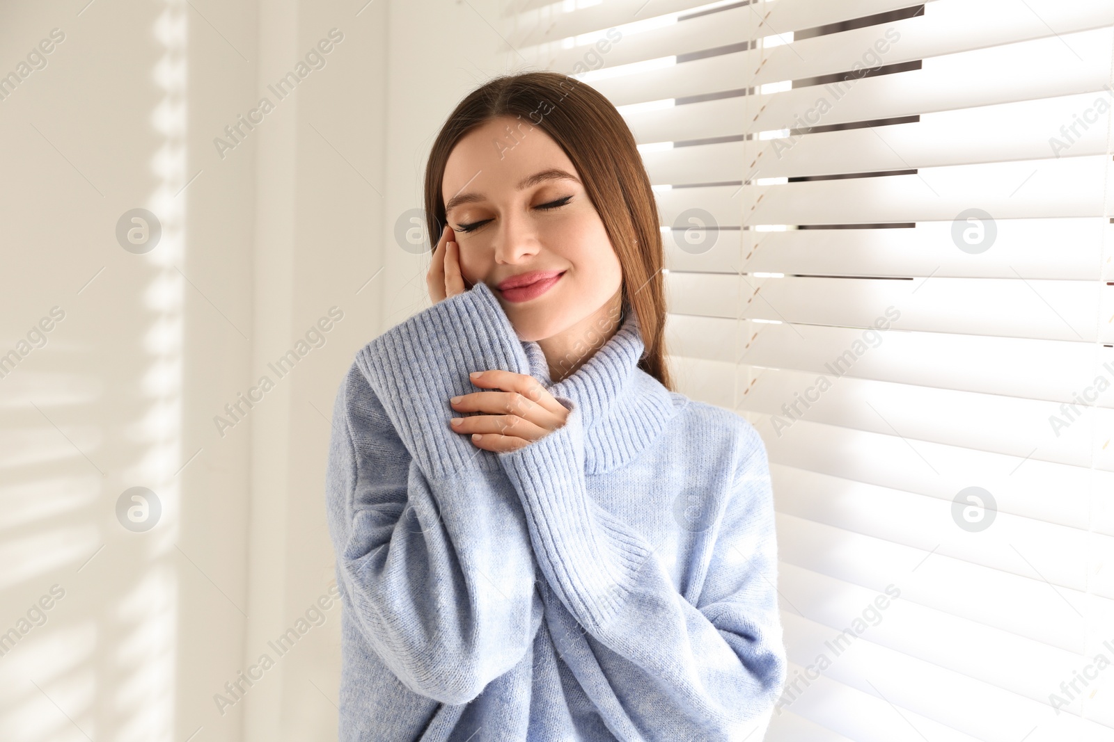 Photo of Young woman wearing warm sweater near window at home. Winter season