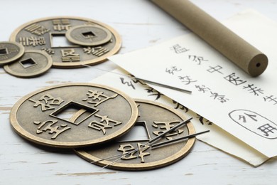 Photo of Acupuncture needles, Chinese coins and sheets of paper with characters on white wooden table, closeup