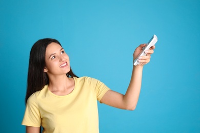 Photo of Happy young woman operating air conditioner with remote control on light blue background