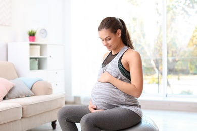 Photo of Young pregnant woman in fitness clothes sitting on exercise ball at home