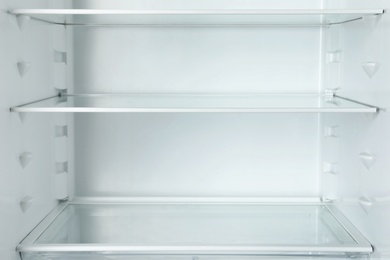 Photo of Modern open refrigerator with empty shelves, closeup