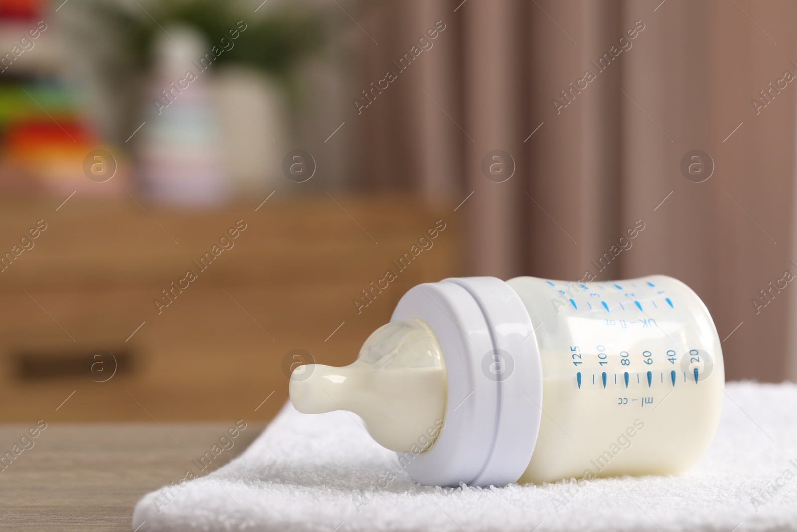 Photo of Feeding bottle with baby formula and soft towel on wooden table indoors. Space for text