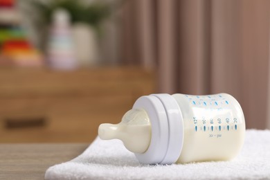 Photo of Feeding bottle with baby formula and soft towel on wooden table indoors. Space for text
