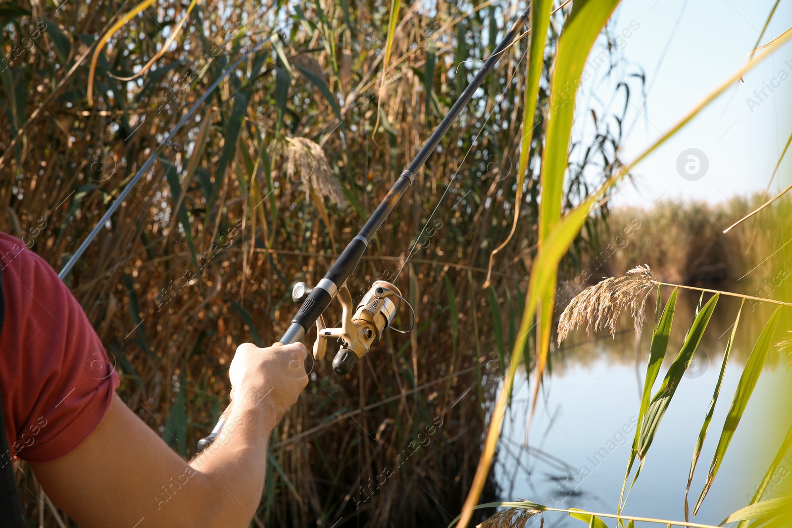 Photo of Man fishing alone at riverside on sunny day, closeup