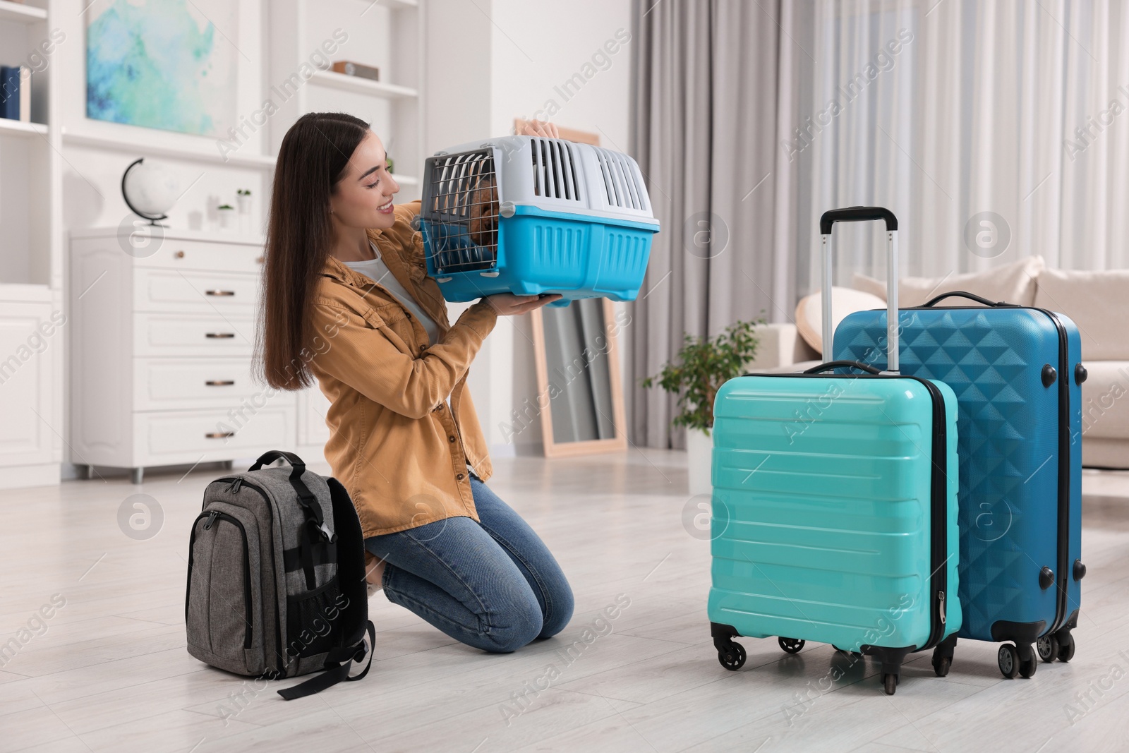 Photo of Travelling with pet. Smiling woman looking at carrier with her dog indoors