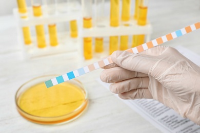 Photo of Laboratory worker holding urine test strip near table, closeup. Urology concept