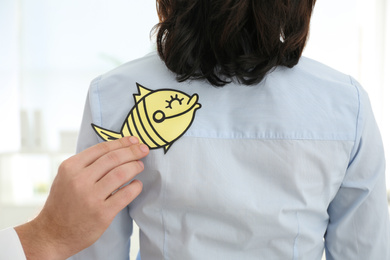 Man sticking paper fish to colleague's back in office, closeup. April fool's day