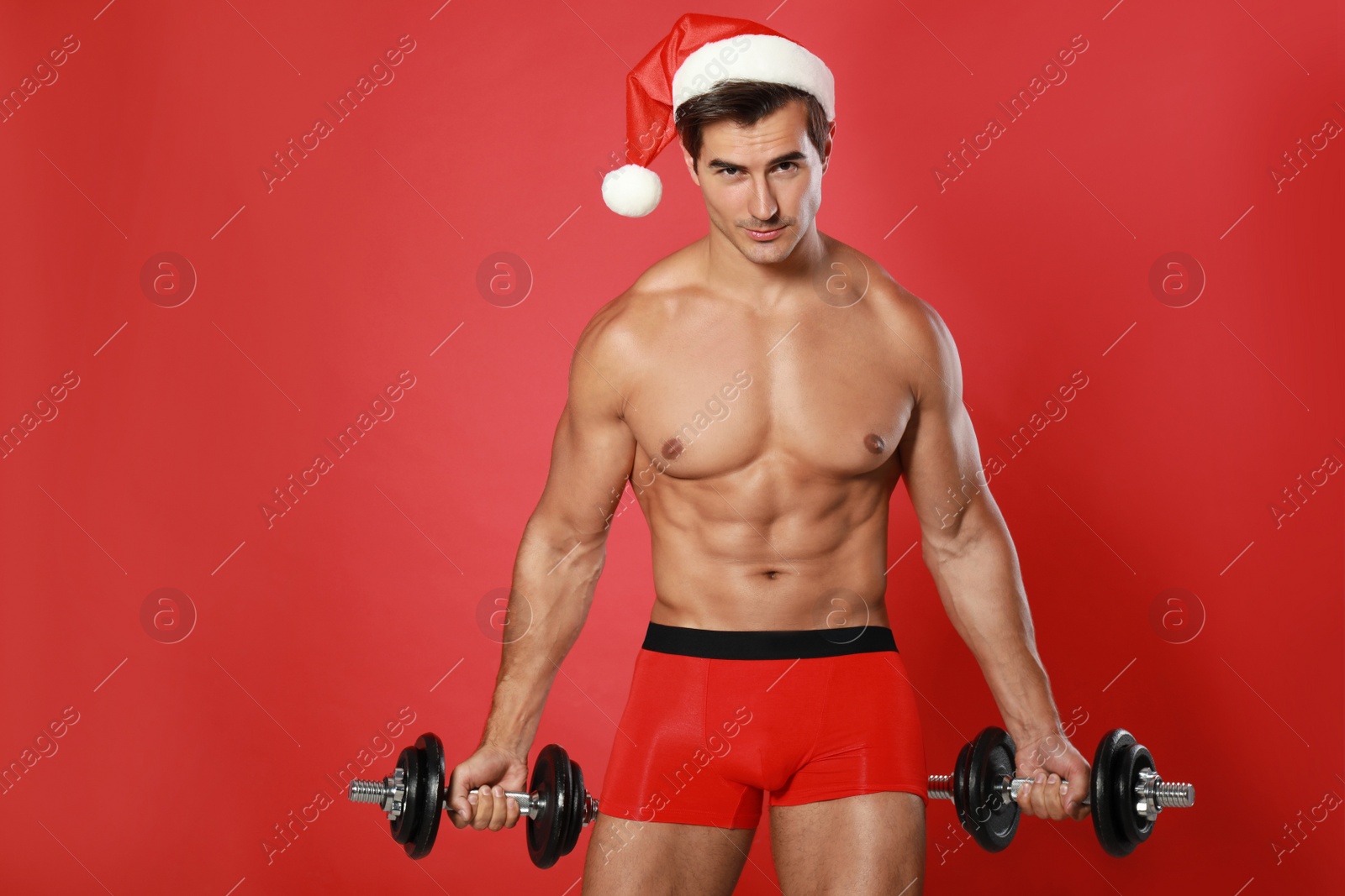 Photo of Sexy shirtless Santa Claus with dumbbells on red background