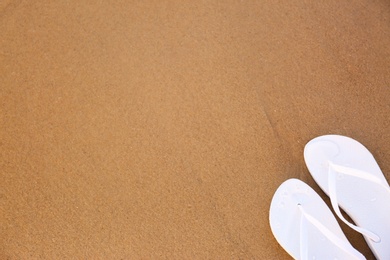 Photo of White flip flops on sand, top view with space for text. Beach accessories