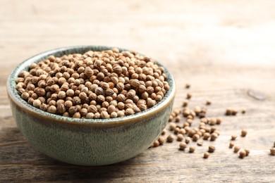 Dried coriander seeds in bowl on wooden table, closeup