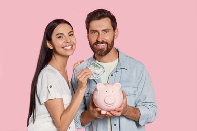 Photo of Happy couple with money and ceramic piggy bank on pale pink background