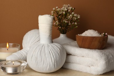 Photo of Composition with different spa products, candles and flowers on beige table against brown background