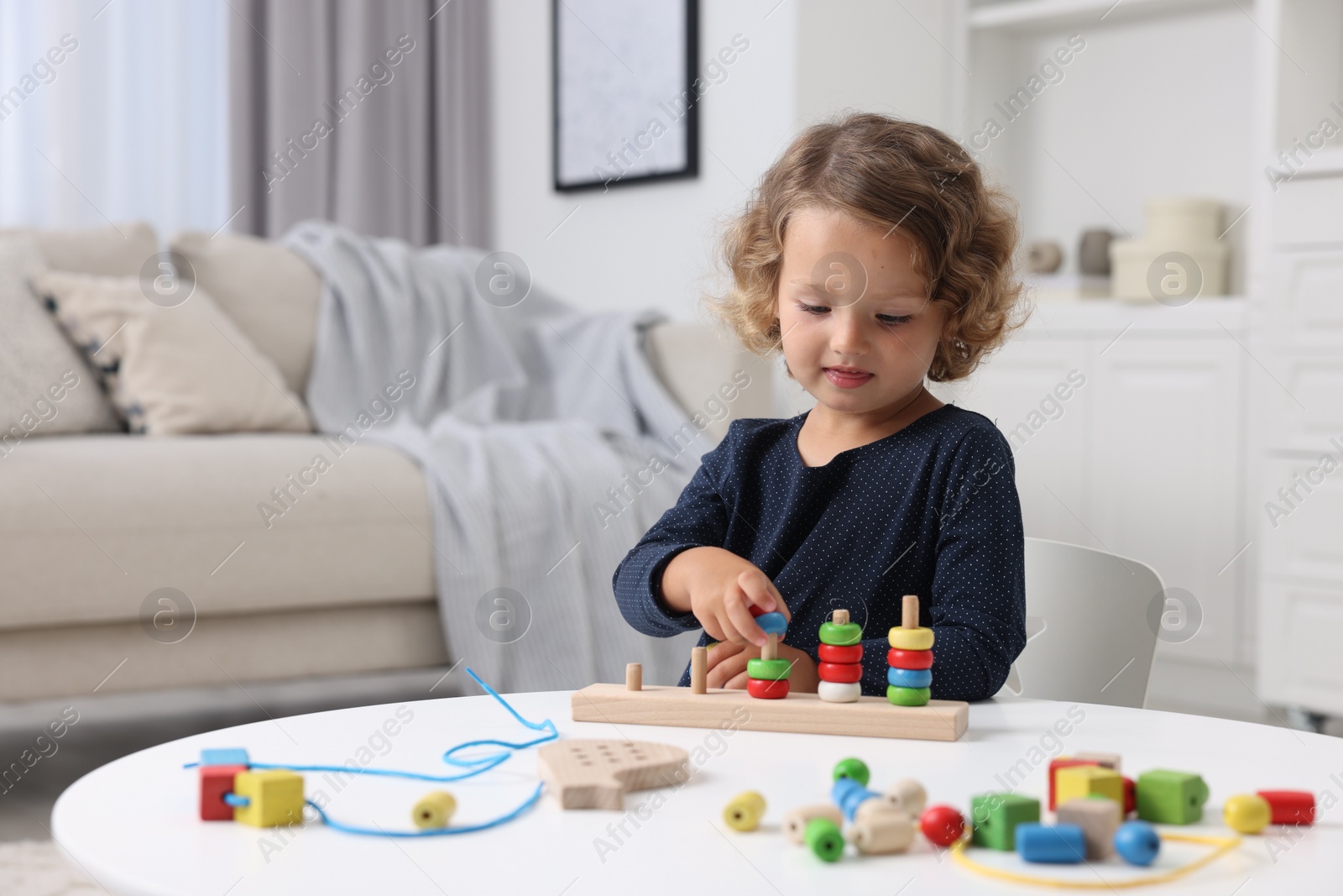 Photo of Motor skills development. Little girl playing with stacking and counting game at table indoors