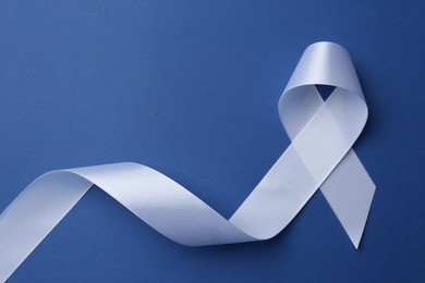 Photo of White awareness ribbon on blue background, top view. Space for text