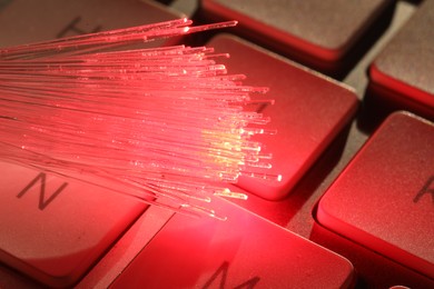 Photo of Optical fiber strands transmitting red light on computer keyboard, macro view