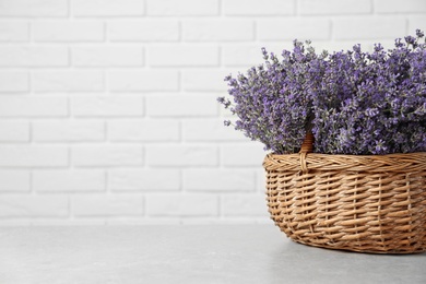 Photo of Fresh lavender flowers in basket on stone table against white brick wall, space for text