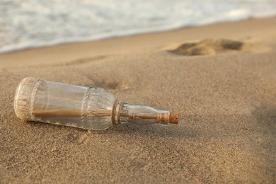 Photo of SOS message in glass bottle on sand near sea, space for text