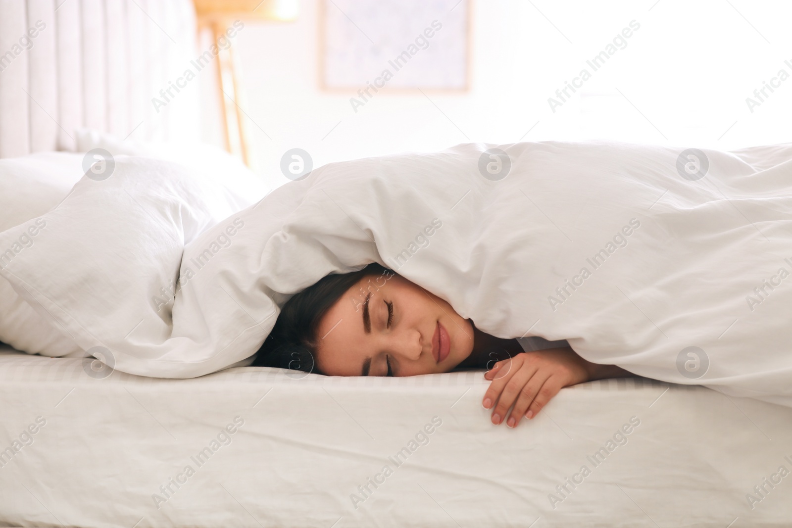 Photo of Young woman covered with warm white blanket sleeping in bed at home