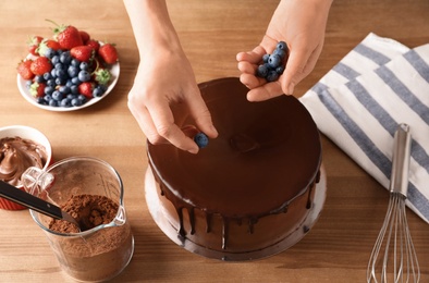 Photo of Baker decorating fresh delicious homemade chocolate cake with berries on table, closeup