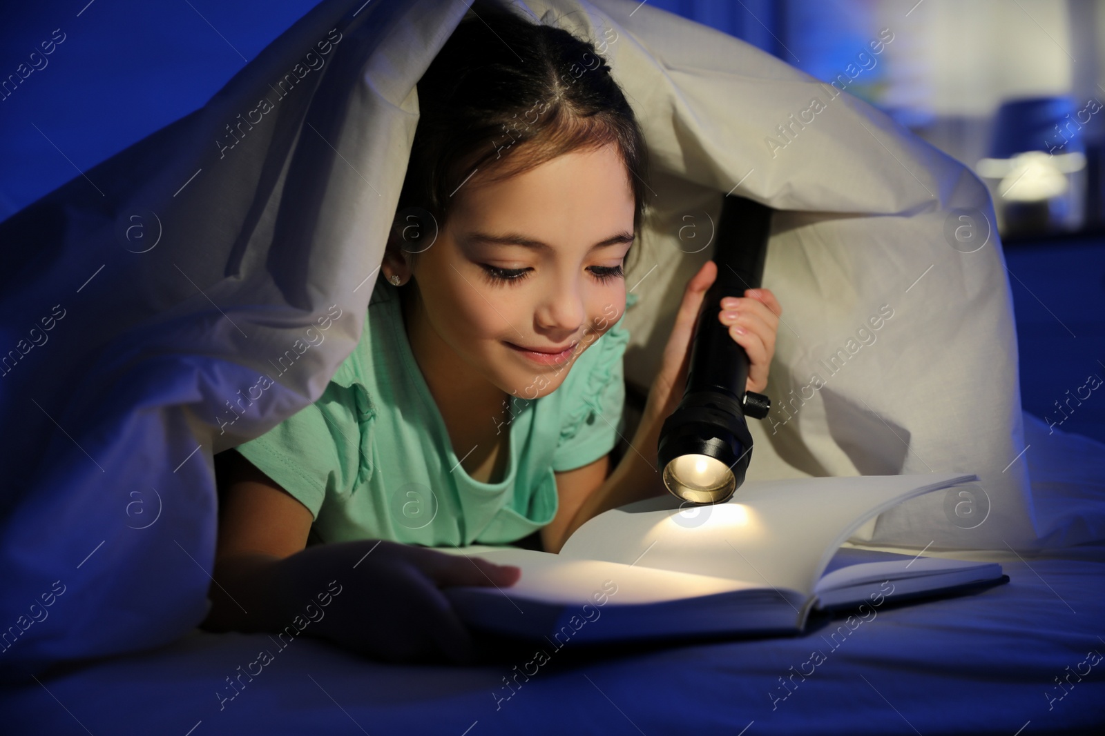 Photo of Little girl with flashlight reading fairy tale in dark bedroom