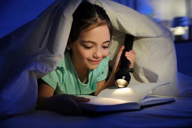 Photo of Little girl with flashlight reading fairy tale in dark bedroom