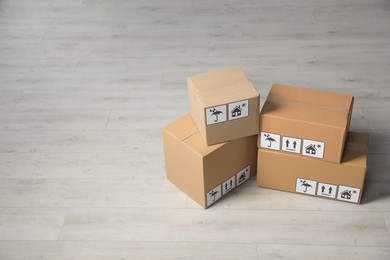 Photo of Many closed cardboard boxes with packaging symbols on wooden floor, space for text. Delivery service